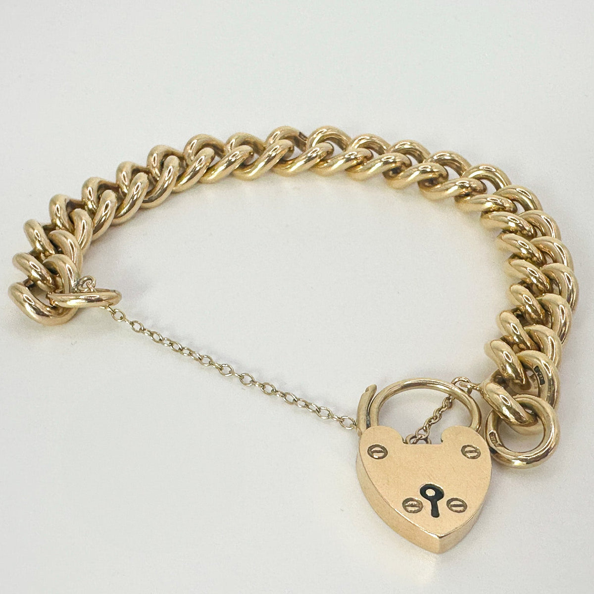 A 9ct yellow gold patterned belcher charm bracelet with a heart-shaped padlock fastener.